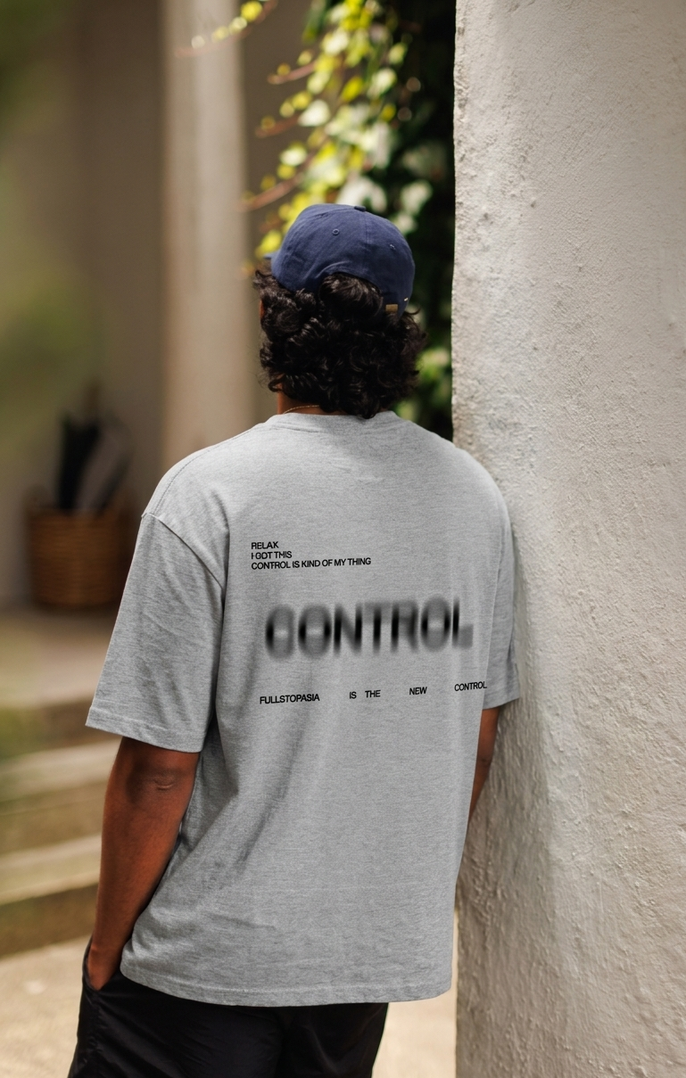 Person wearing a gray t-shirt with 'CONTROL' printed on the back, leaning against a wall.